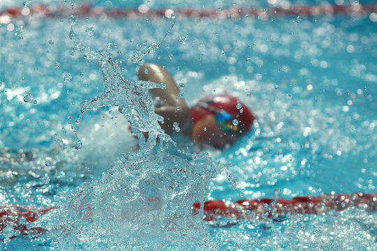 Blurred image of swimmer wearing red swimming cap, focus to water splash