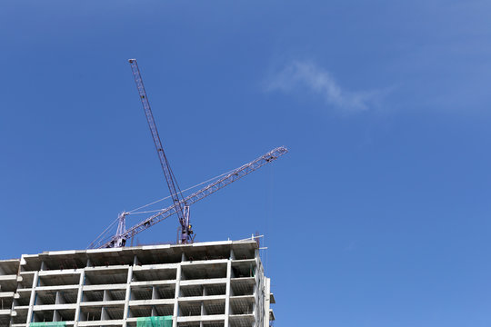 Crane working on a building under construction in day time.