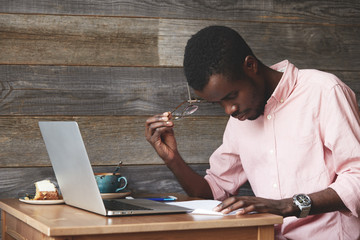 Portrait of thoughtful and concentrated young African American copy-writer, dressed in pink shirt,...