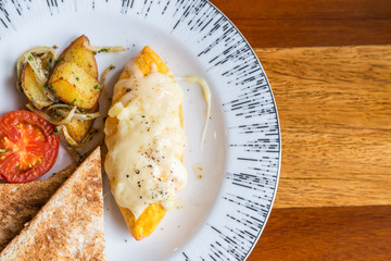 Omelet with potato, tomatoes parsley and feta cheese and bread in white plate on wooden table. Soft focus