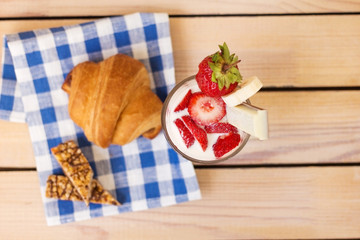 milkshake with strawberries and blueberries, baked croissant on a wooden background