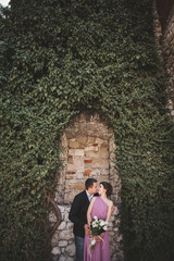 Fototapeta na wymiar Luxury wedding couple hugging and kissing on the background gorgeous plants, cave near ancient castle