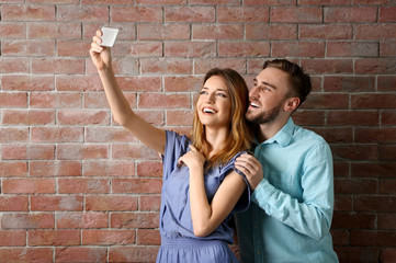 Young cheerful friends taking selfie on brick wall background