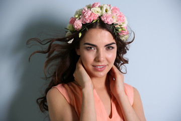 Fototapeta premium Beautiful young woman with flowers on head on light background