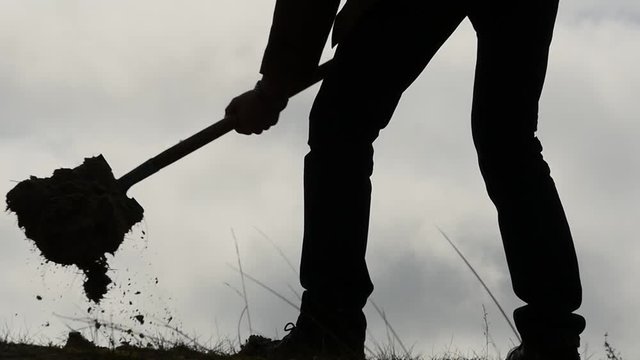 silhouette of man digging a hole with a shovel slow motion close up