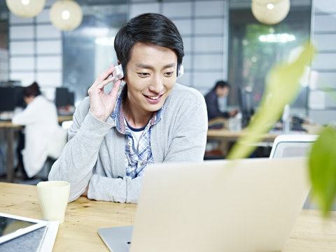 young asian designer listening to music while working in office