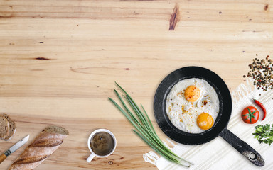 Farmers breakfast. Frying pan with two fried eggs, tomato, green onion, chili and black pepper, bread and coffee on aged wooden table. Top view with copy space