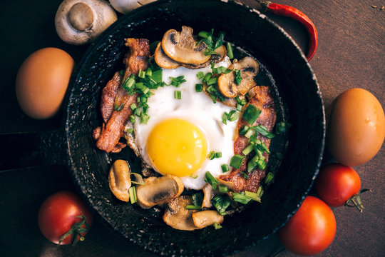 old pan. fried egg, bacon, mushrooms, green onion - tasty Breakfast or snack. On a dark wooden table. Top view