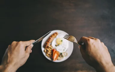 Photo sur Plexiglas Oeufs sur le plat Male hands holding silver cutlery over out of focus plate, on the plate there is fried egg with sausage