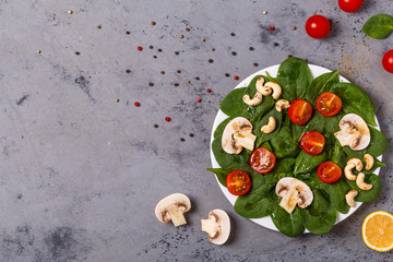 Salad with spinach, mushrooms and tomatoes on concrete backgroun