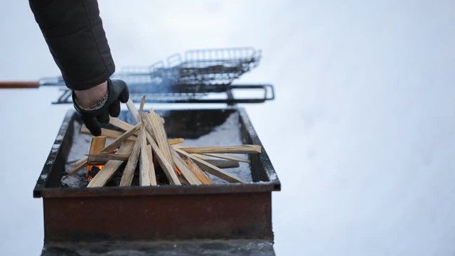 Man in the winter watching fire erupted in grill and puts him in kindling.