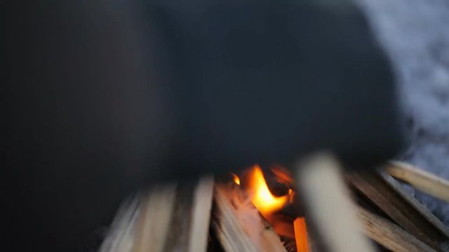 Man in winter watching fire putting new stick to it.
