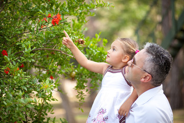 A father holding his daughter in his arms, hugging her and shows garden flowers and fruits