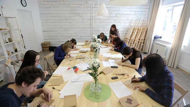 People sit around wooden table and draw some pictures in studio