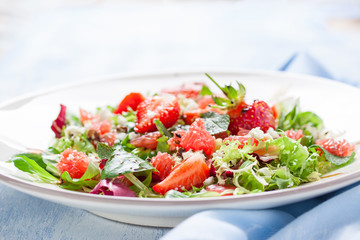 Summer salad with grapefruit, strawberry, mint, balsamic and cheese on a plate on a wooden background, closeup
