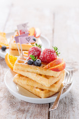 Homemade waffles with fruits, syrup and sugar on a white plate on a wooden background, closeup..