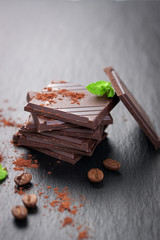 Stack of chocolate chunks with mint on a dark stone background with cocoa, closeup