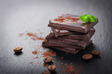 Stack of chocolate chunks with mint on a dark stone background with cocoa, closeup, horizontal with...