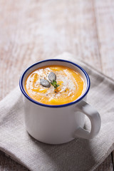 Homemade tasty creamy pumpkin soup puree in a bowl on a wooden background.