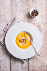 Homemade tasty creamy pumpkin soup puree in a bowl on a wooden background, top view.