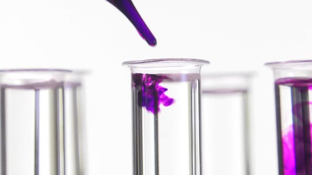 pipette depositing drops of purple  dye in rotating test tubes