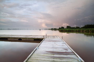 wooden pier on lake during shower at sunset