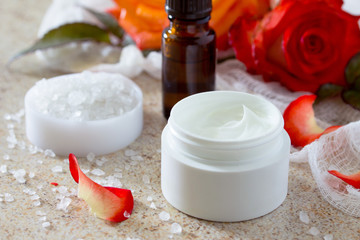 Face cream with roses, bottle of aromatherapy essential oil and