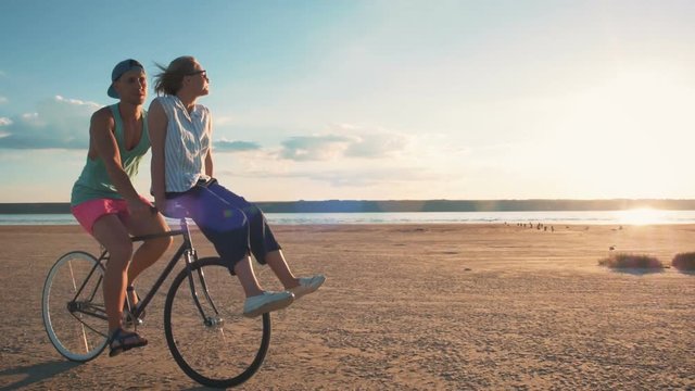 Young woman and man riding a bicycle at the shore and having some fun, slow motion
