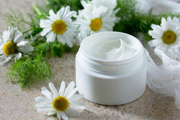 Face cream with chamomile on a brown stone background - beauty s