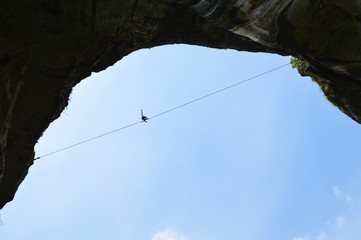 Silhouette of vertical cliffs, young highline walker on a tightrope high in the blue sky