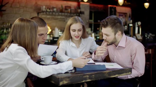 Half length of young business men and women sitting in a bar discussing something