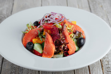 Salad of fish with olives, cucumbers and tomatoes in the white plate on a wooden table