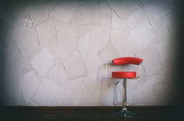 modern red chair in an empty room. in the circle of light there is red swivel chair on a background of gray wall with decorative relief plaster. copy space for your text