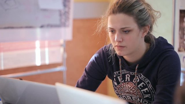 Beautiful blonde woman in a hoodie working on a laptop