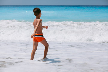 Beach vacation dream. Handsome young boy enjoying in beautiful tropical beach, running and playing with waves.