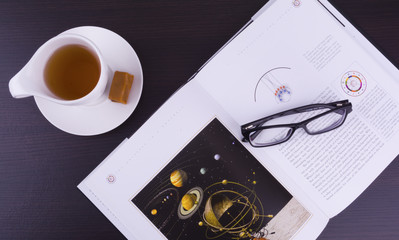 An open book, a cup of tea, glasses and on the wooden background