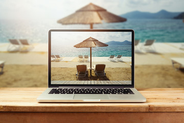 Laptop computer with sunny beach image on wooden table. Summer vacation photo sharing
