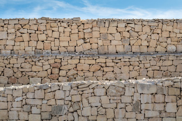 Limestone layered, rough dry stone wall, under a blue sky.