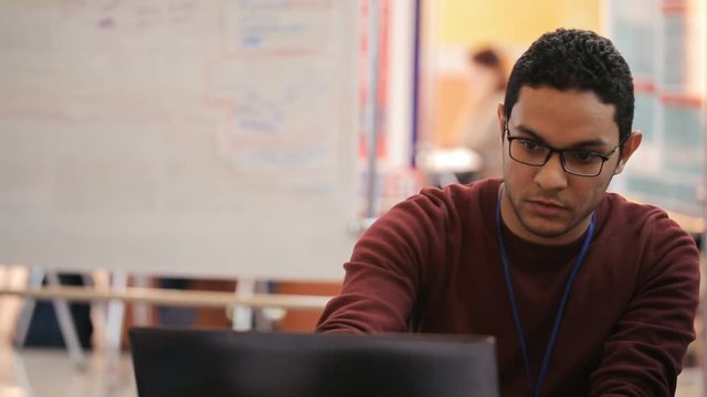 A very serious young man in glasses looks at the laptop screen