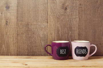 Coffee cups on wooden table with chalkboard sign and best friends text. Friendship day celebration background