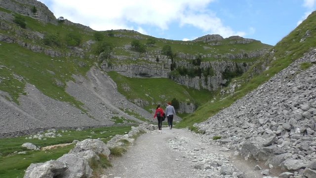 Rear view of young woman and man talking while walking on the stone track by loose limestone scree slopes in North Yorkshire Pennine mountain area
