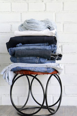 Denim clothes and blue scarf stacked on a cutty stool against the white brick wall