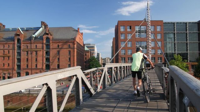 4K UHD Hamburg Speicherstadt Kehrwiedersteg, male man walking over bridge with bicycle in real time, Germany