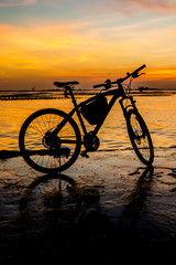 Fototapeta premium Silhouette of bicycle at jetty with sunset sky and sea backgroun