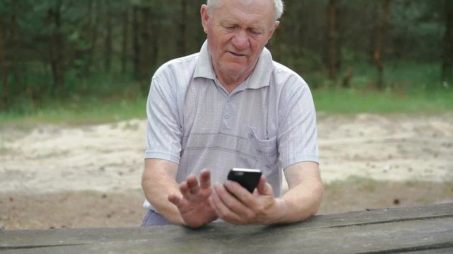 The old man with wrinkles uses the phone in the forest