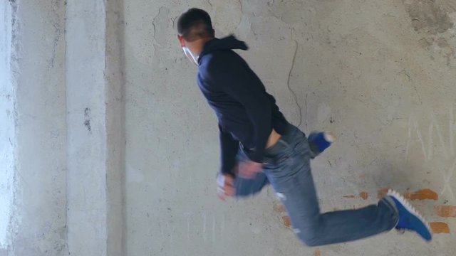 A young man back flips off a wall. Slowly