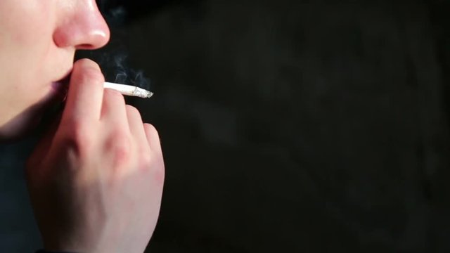 Close up of a human hand holding a smoking cigarette on a black background