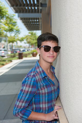 Short haircut female teen in sunglasses leaning close to store wall.
