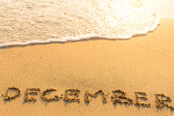 December - inscription on sand beach with the soft wave..