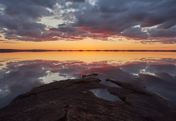 Obraz premium Sunset with crimson red color in the clouds and the rocks on the shore. Dramatic reflection of the sunset in the still water of a lake in Finland.